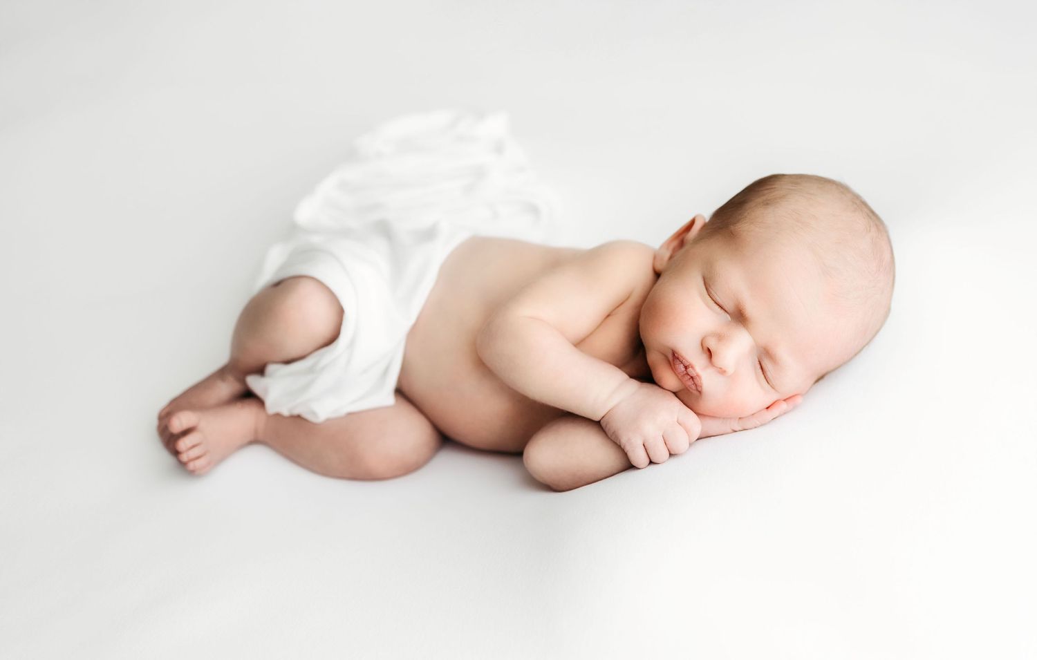 Sleeping newborn baby lying on a white background wearing a cloth diaper.