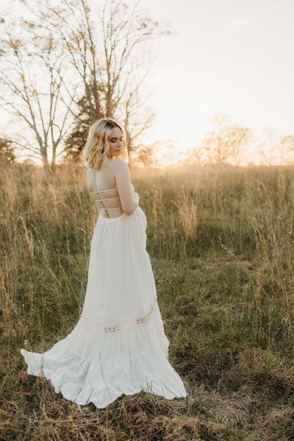 A backlit white dress flows elegantly against tall grass during sunset.