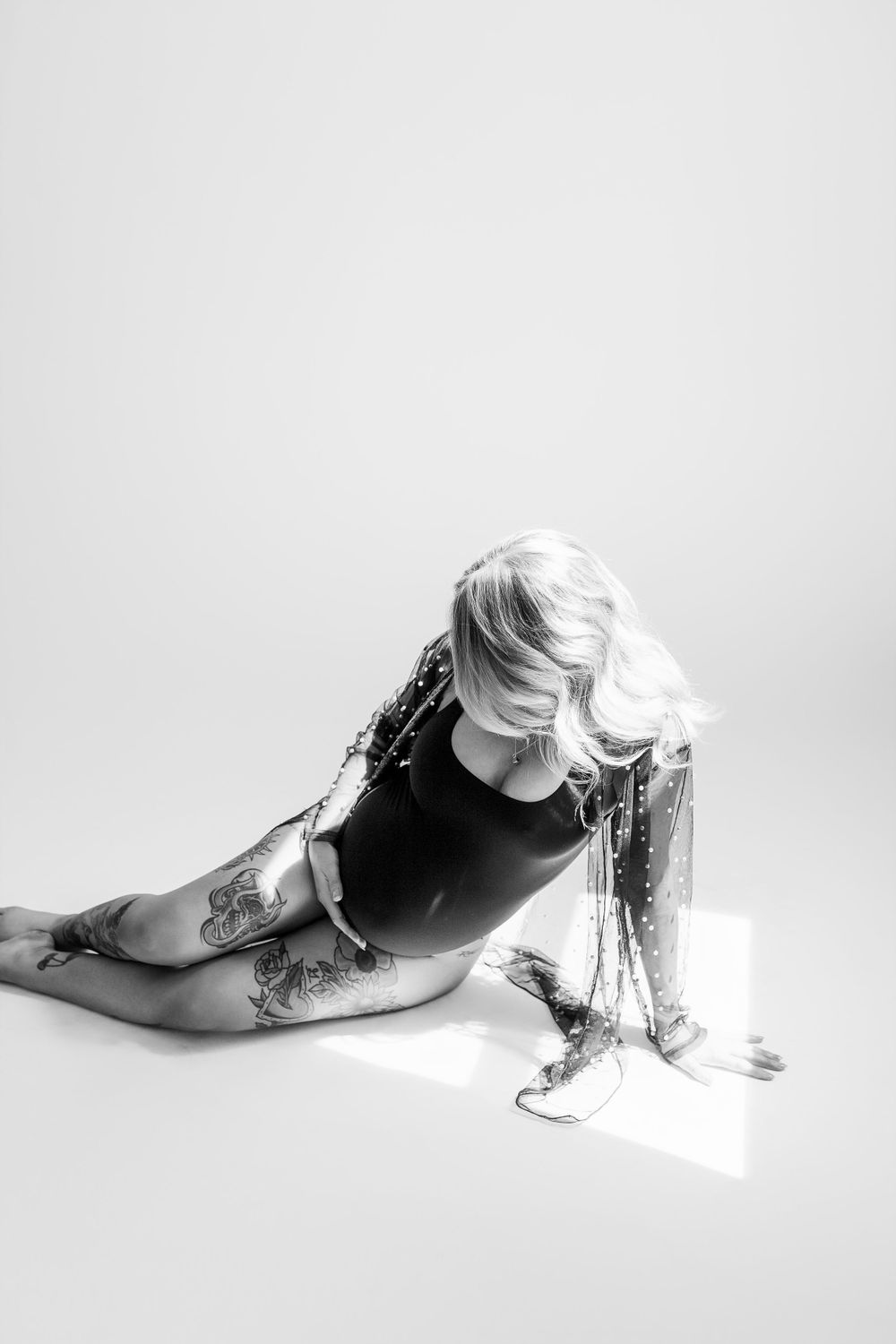 Black and white artistic portrait of someone in a leotard with tattoos laying on floor with dramatic silver tinsel elements.