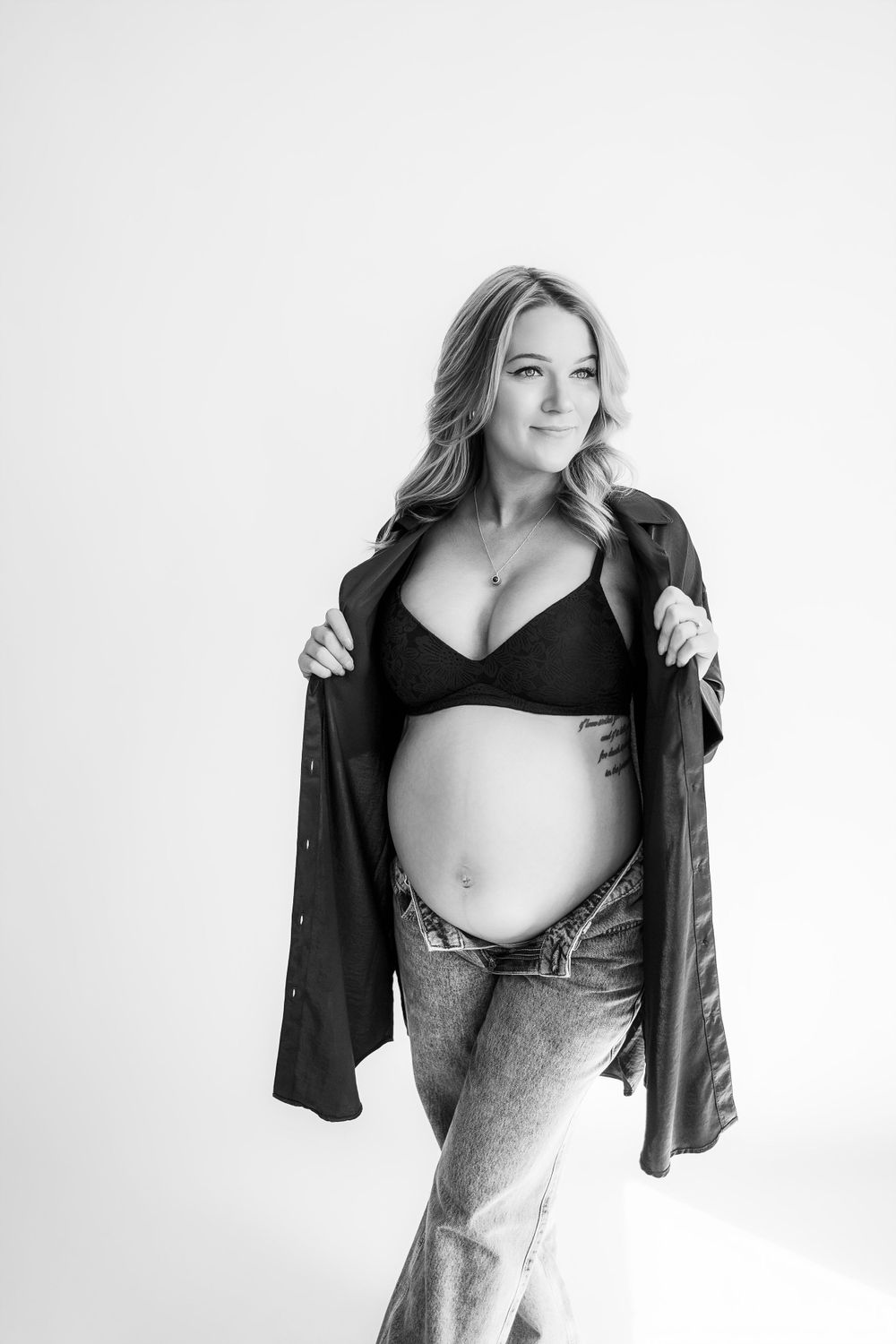 Black and white maternity portrait showing an expectant figure in casual denim and black top.