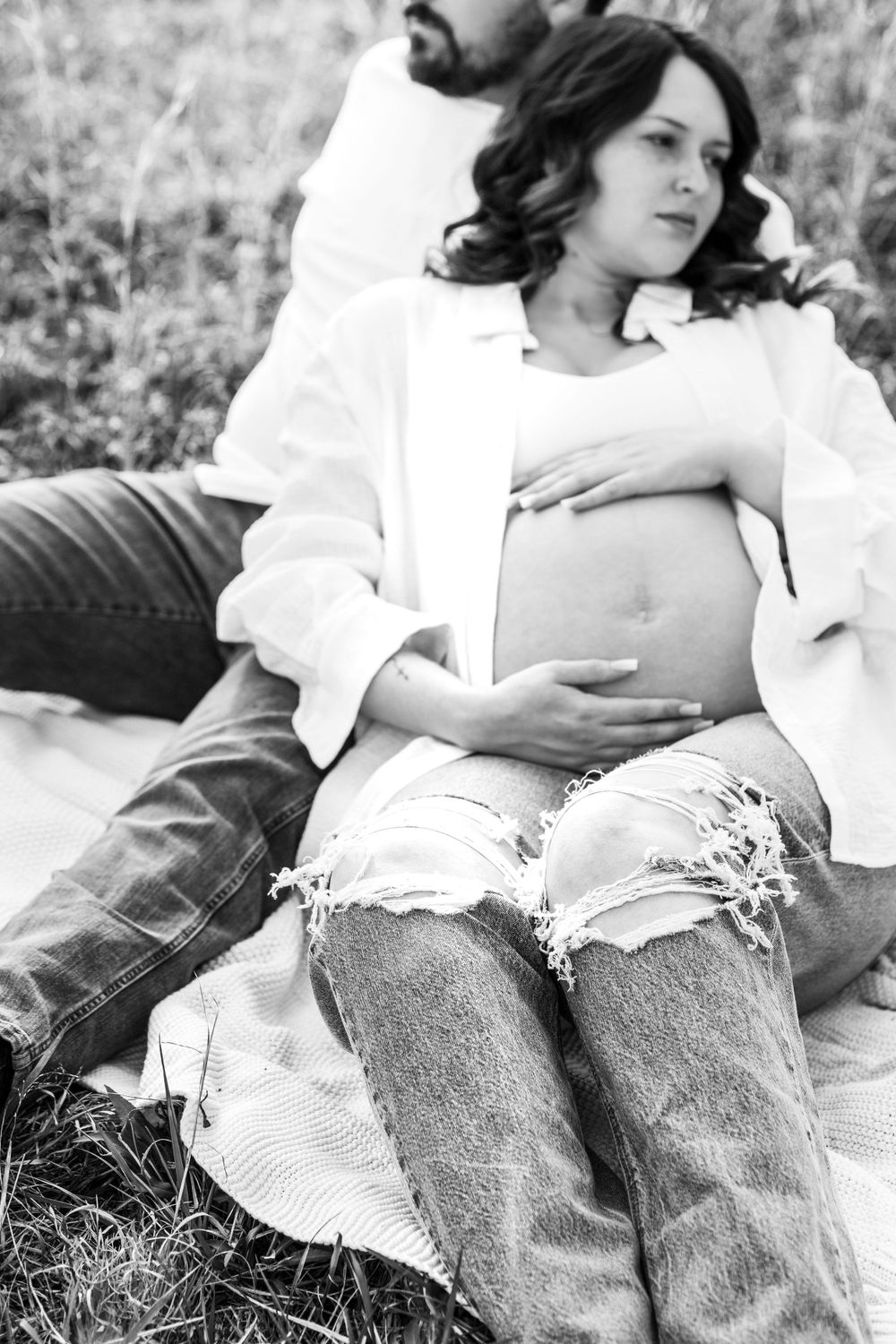 Black and white maternity portrait of couple relaxing outdoors.