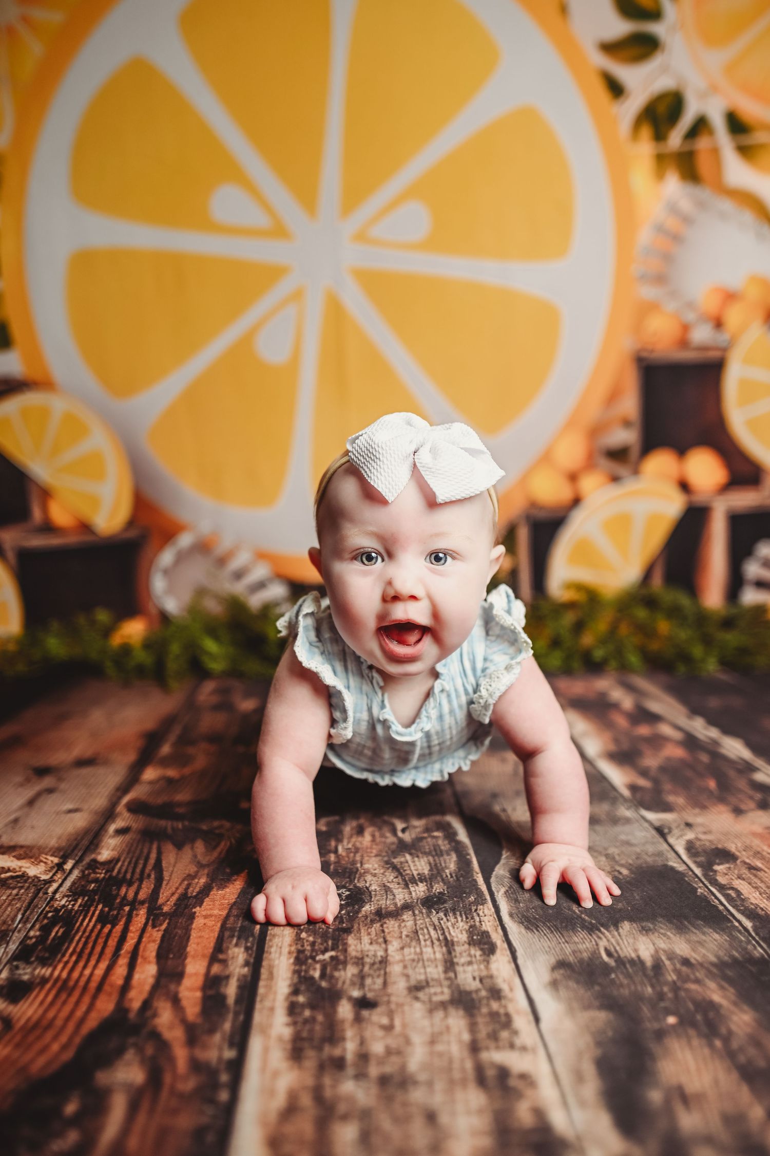 Baby in a floral dress crawls on a rustic wooden floor with a yellow floral backdrop.