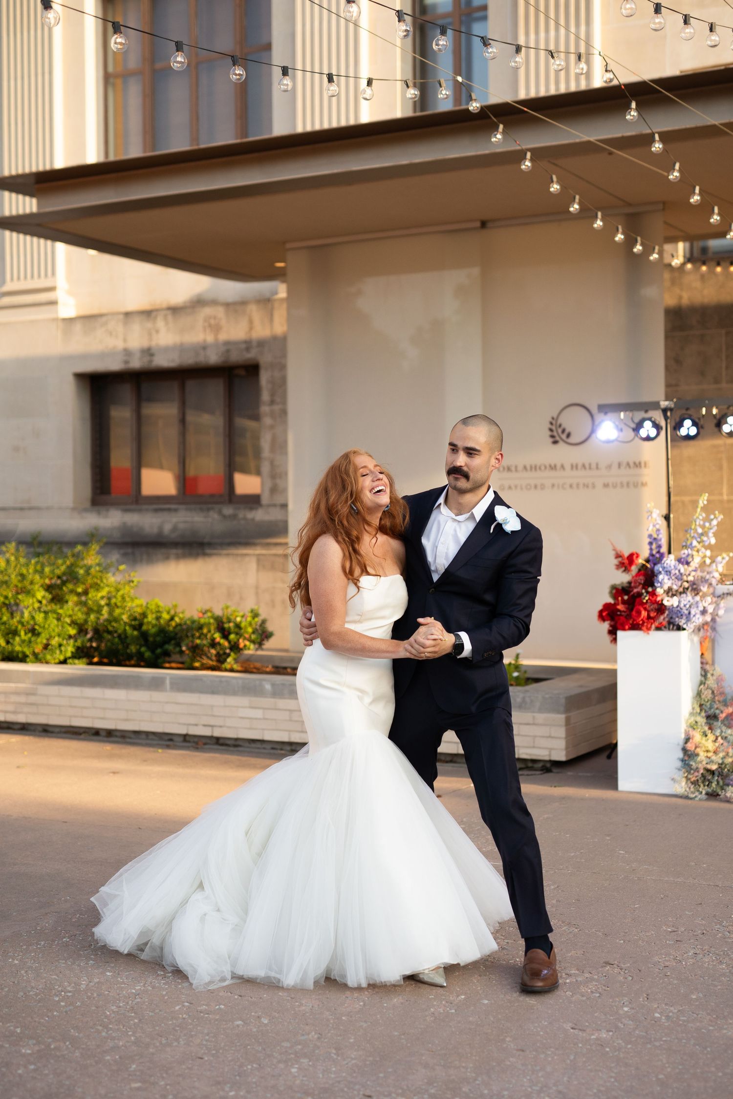 Couple dancing together under string lights, bride wearing a flowing white ballgown.