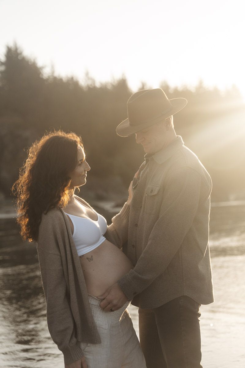 Side profile silhouette of an expectant couple embracing at sunset against a lakeside backdrop.
