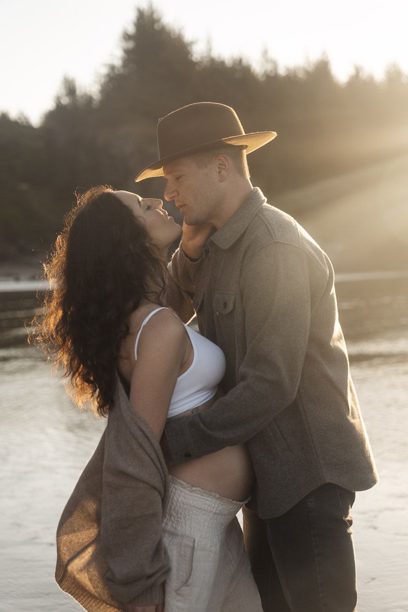 A couple embraces tenderly on a beach during golden hour with beautiful lens flare and backlighting.