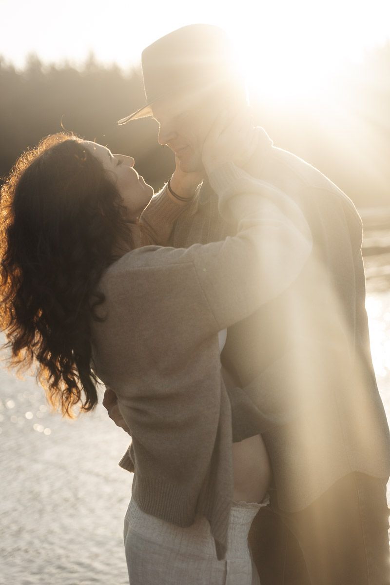 Romantic couple embracing closely in dreamy backlit sunset light on a beach with sun flare filtering through the scene.