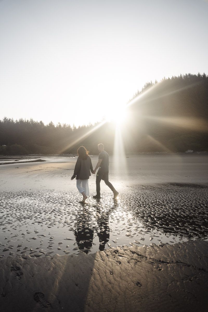 Silhouettes of two people walking hand in hand on a beach with dramatic sunset lighting and rippled sand.