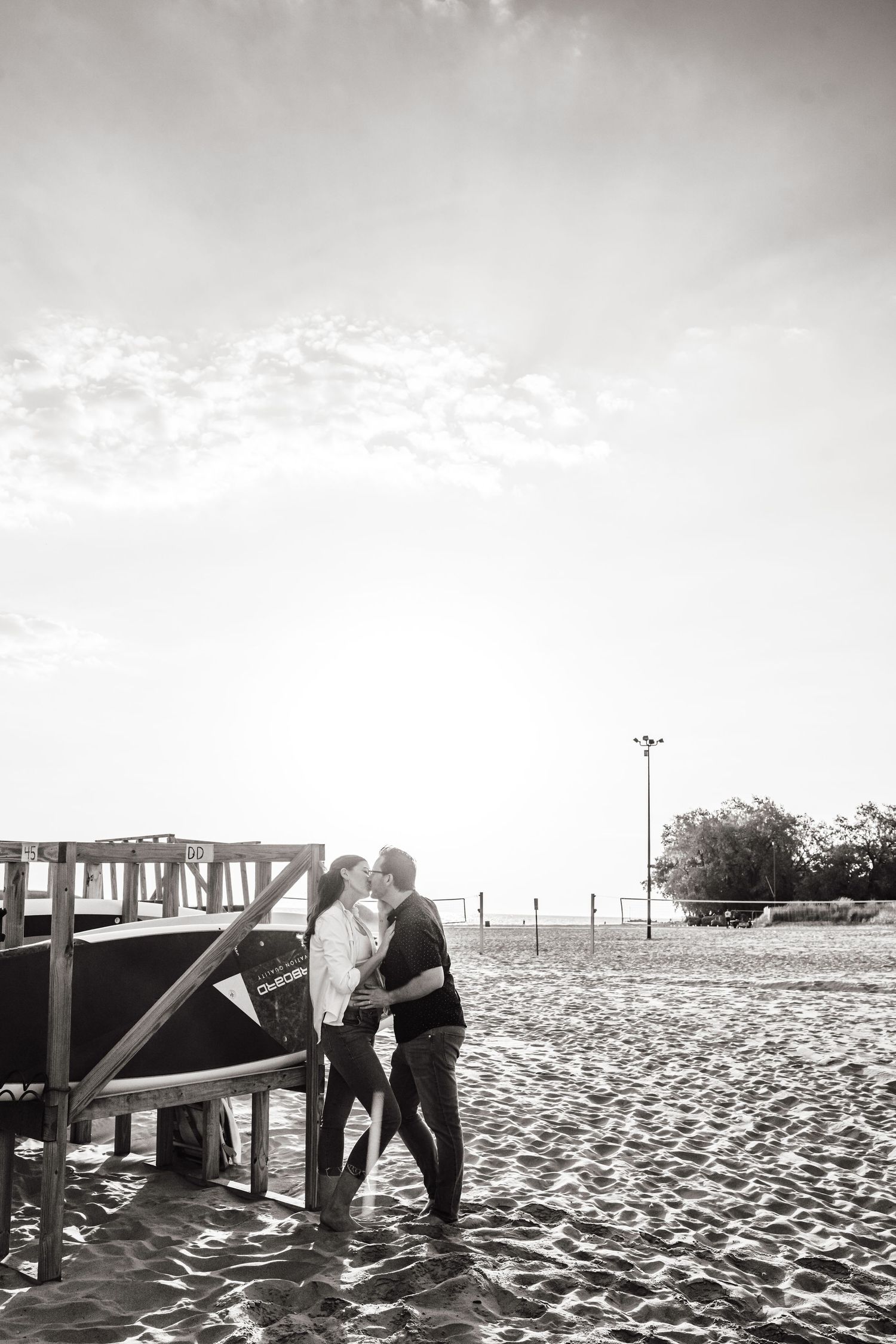 Couple embracing near wooden dock on sandy beach in black and white photography.