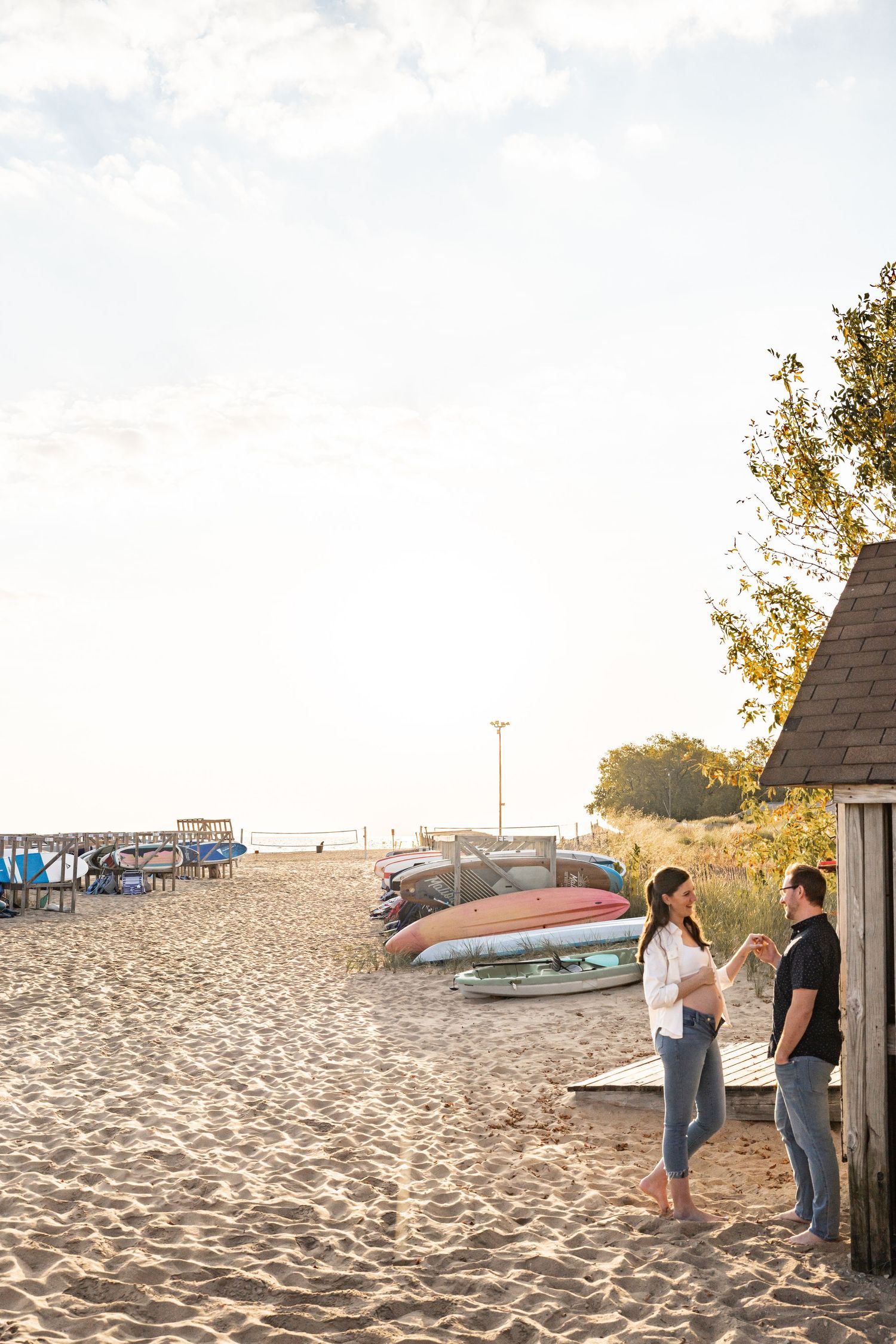 Couple talking and laughing together on sandy beach beside rustic wooden hut with boats.