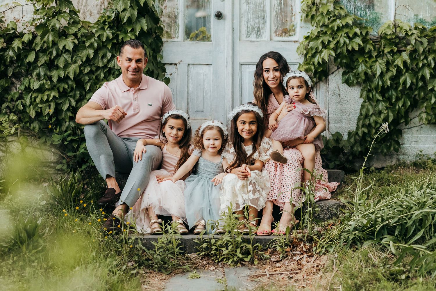 A group enjoys a playful moment together in a sunny garden with blooming flowers and trees in the background.