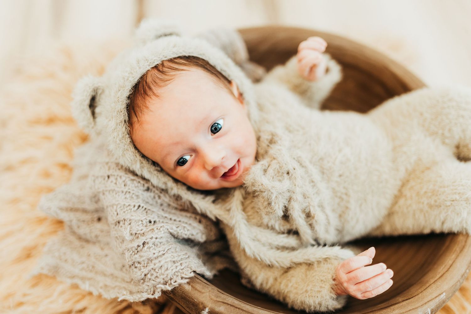 Newborn wrapped in white swaddle lying on fluffy cream-colored blanket.