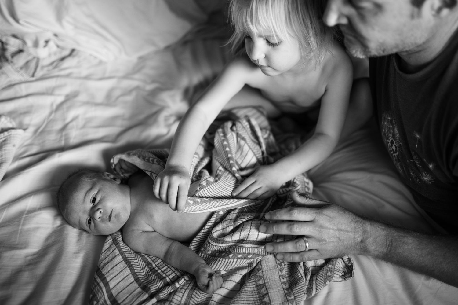 Color photograph of a baby looking at the camera with his mama nuzzling into his face.