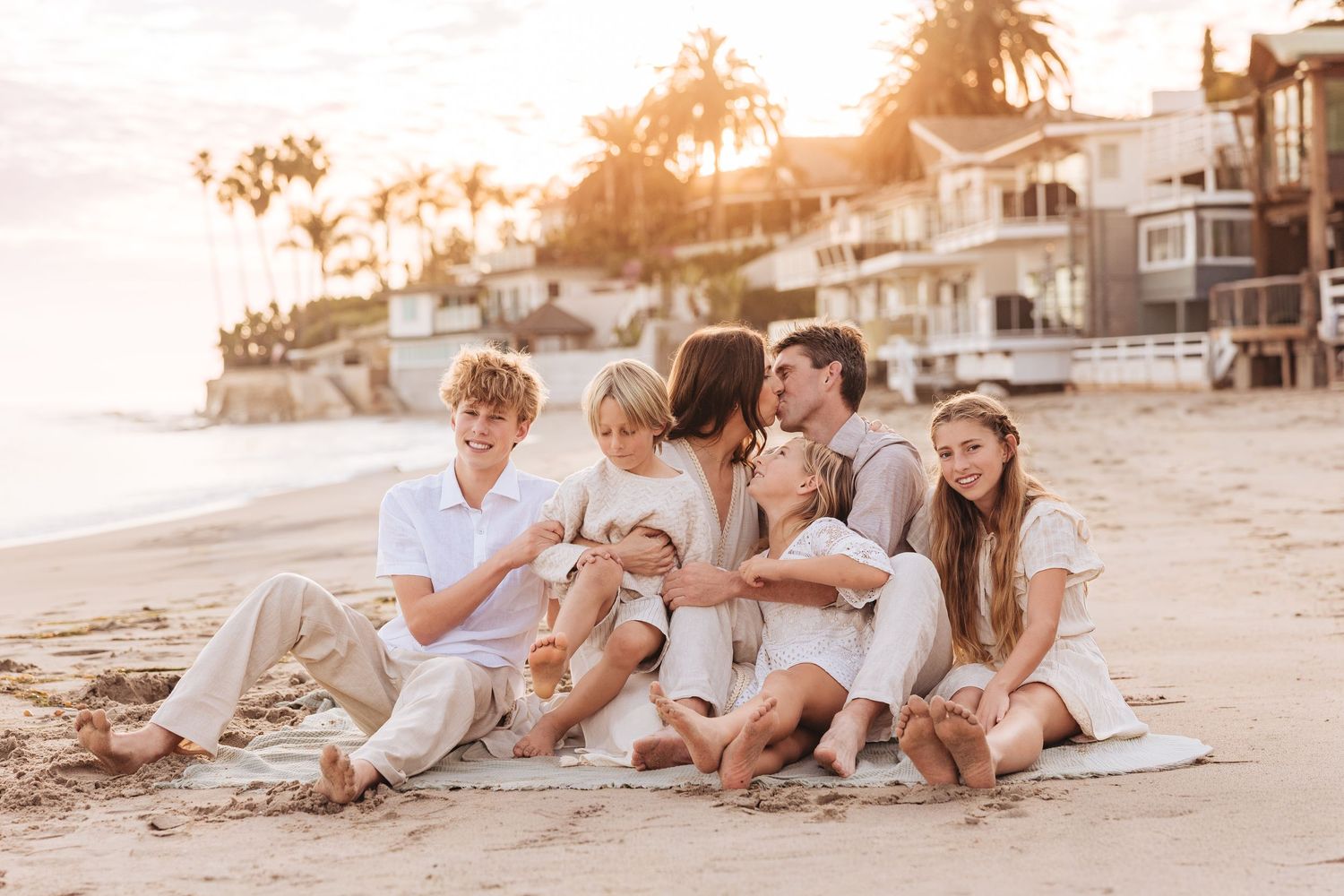 A happy family enjoying quality time together while sitting and playing on a sandy beach at sunset.