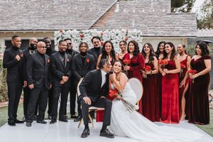 Wedding party poses together in formal attire with bridesmaids in red dresses and groomsmen in black suits.
