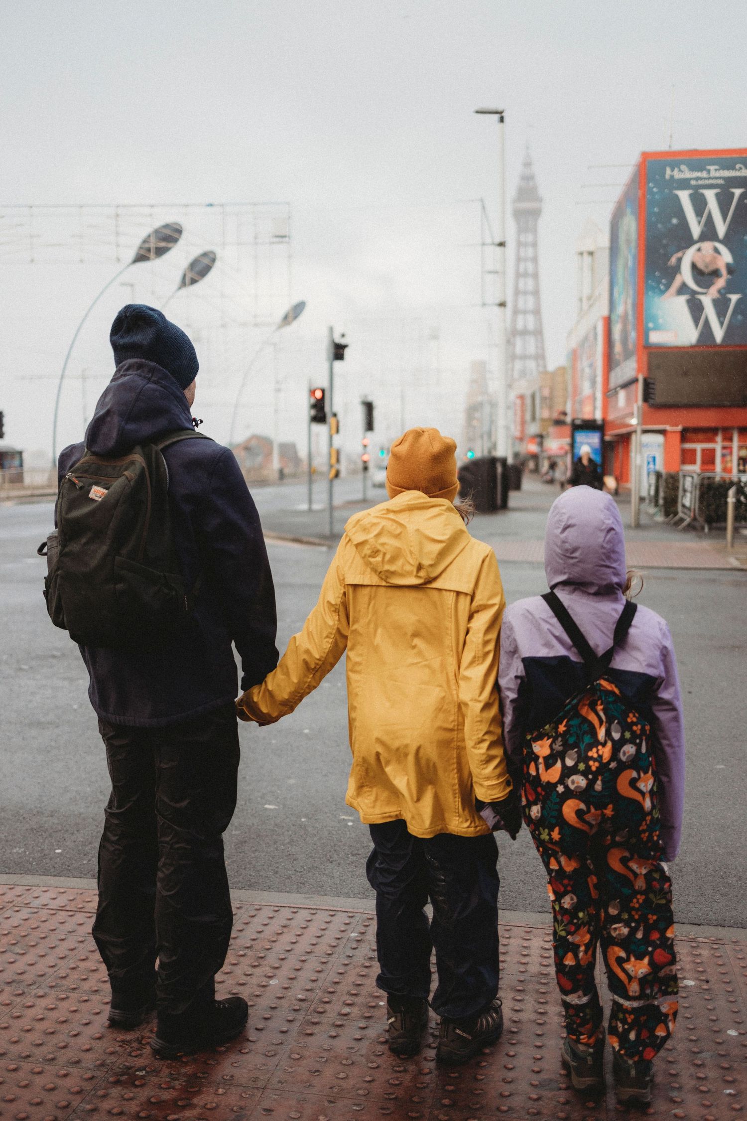 Three people in winter coats standing on a rainy city street.