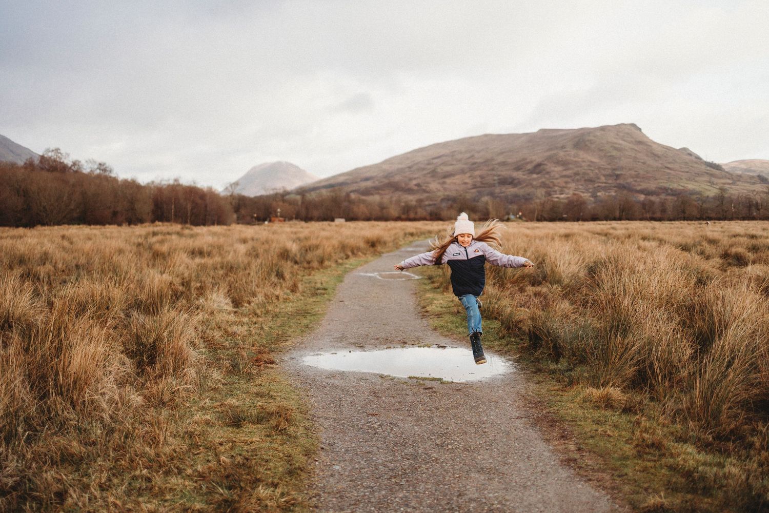 Person skipping joyfully along a path through golden autumn grasslands with mountains in background.