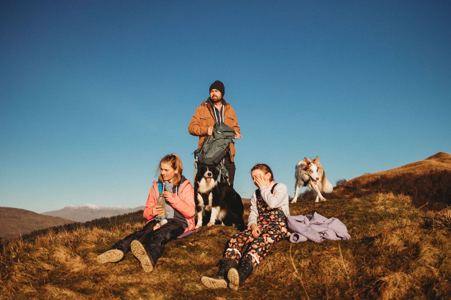 Group sitting together on rocky hillside with dog during sunny afternoon.