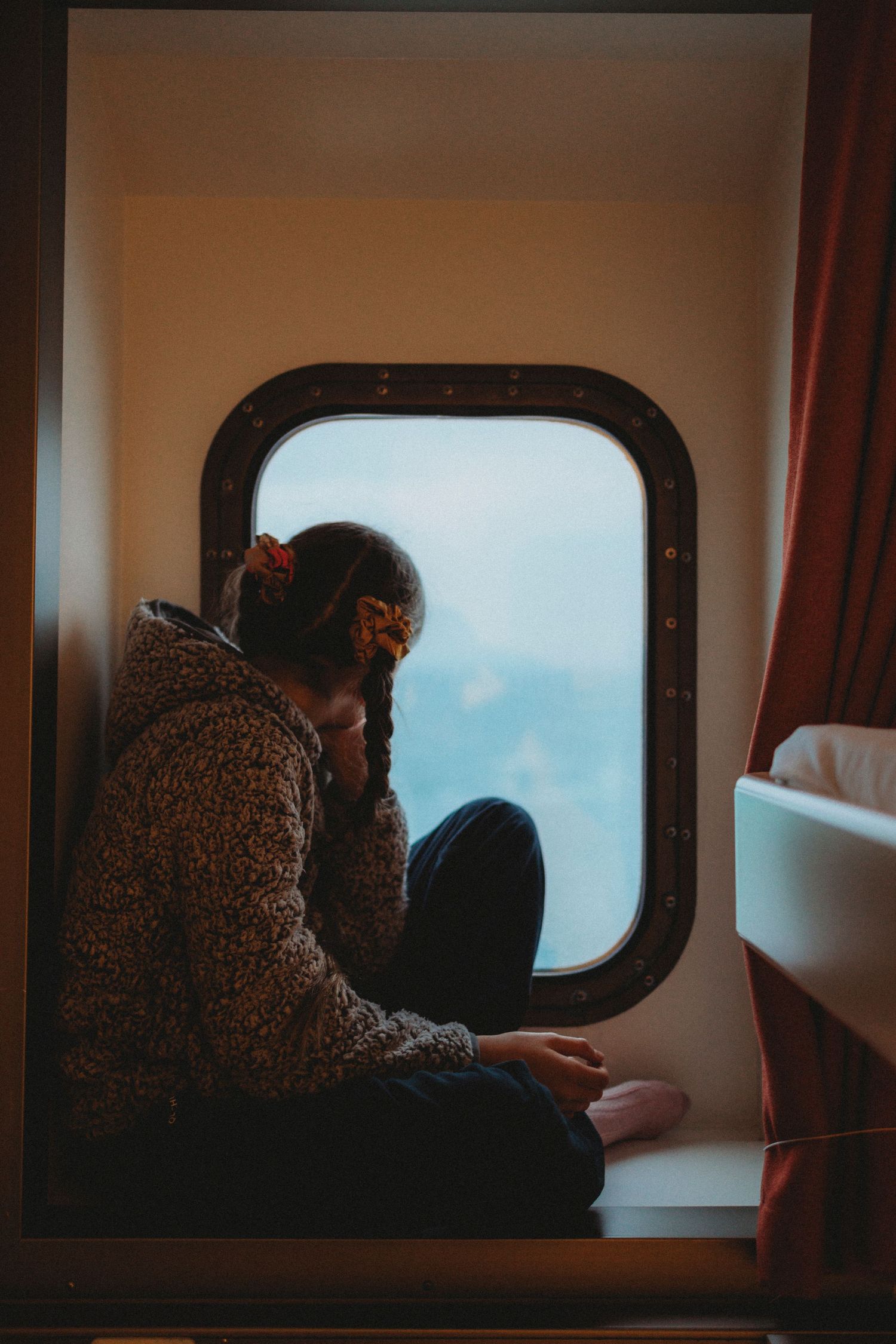 Person in fuzzy sweater sits by airplane window looking out at blue sky.