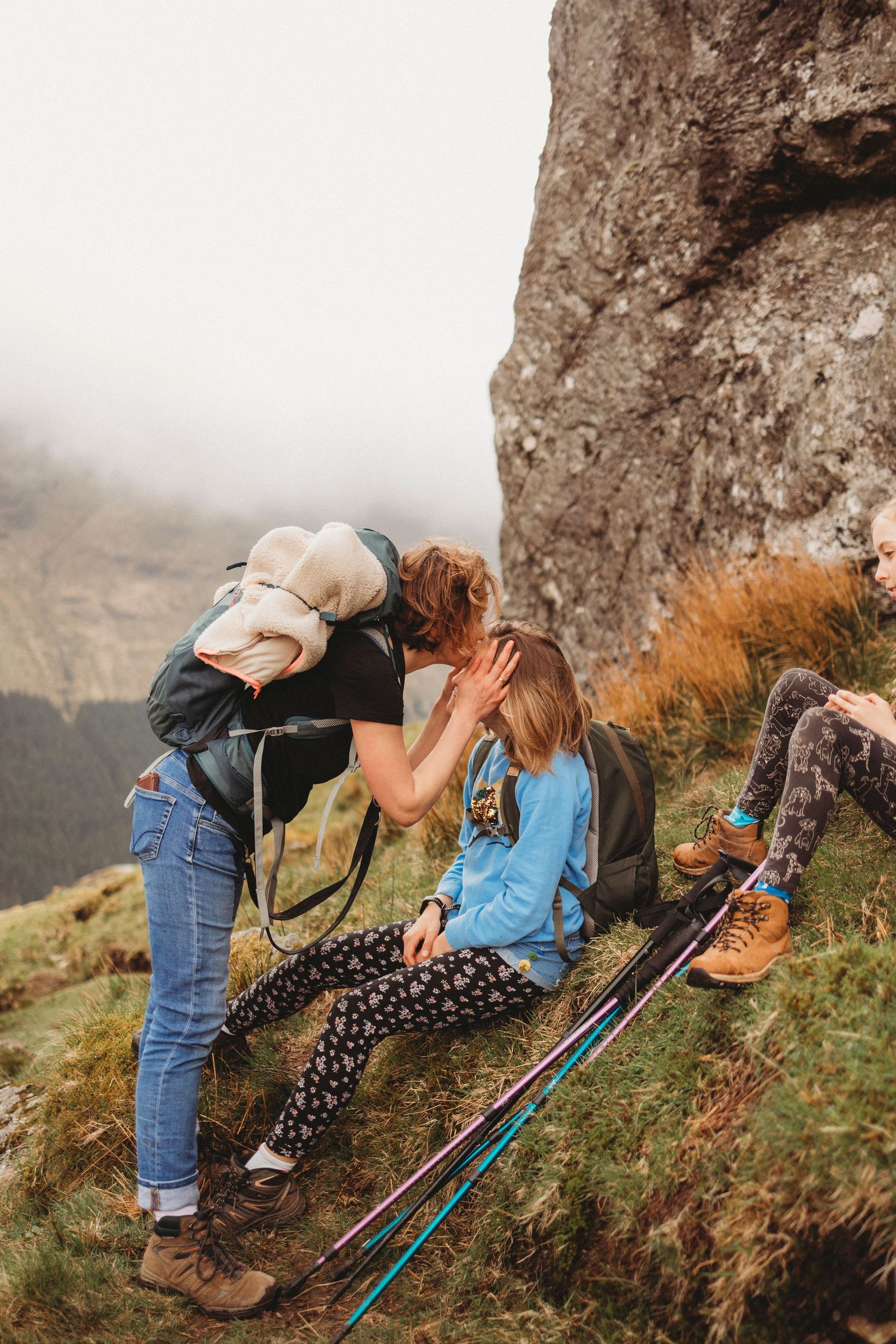 Hikers taking break on mountain trail with hiking poles and backpack visible.