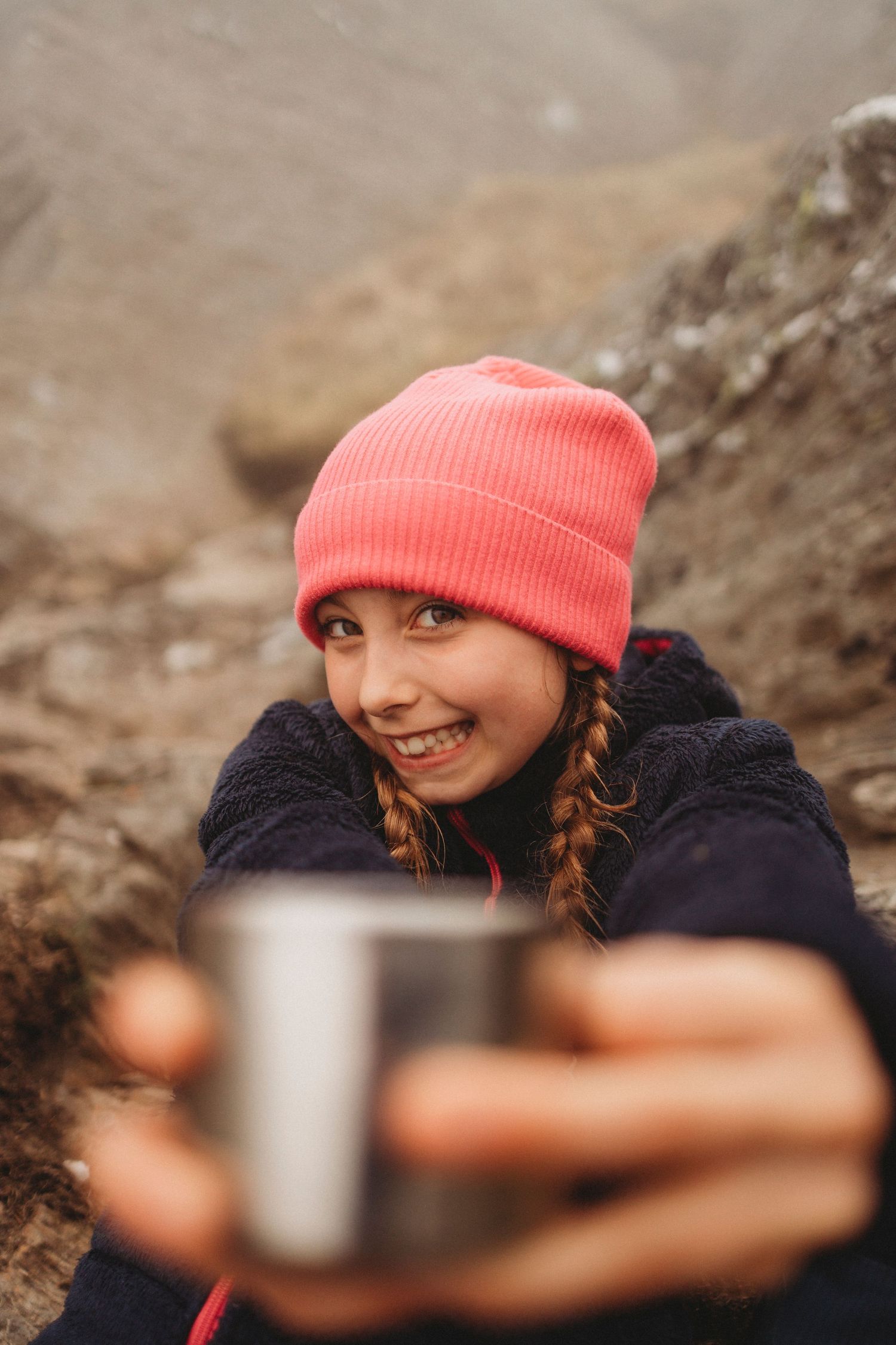 Person in coral beanie holding metal mug while hiking outdoors.