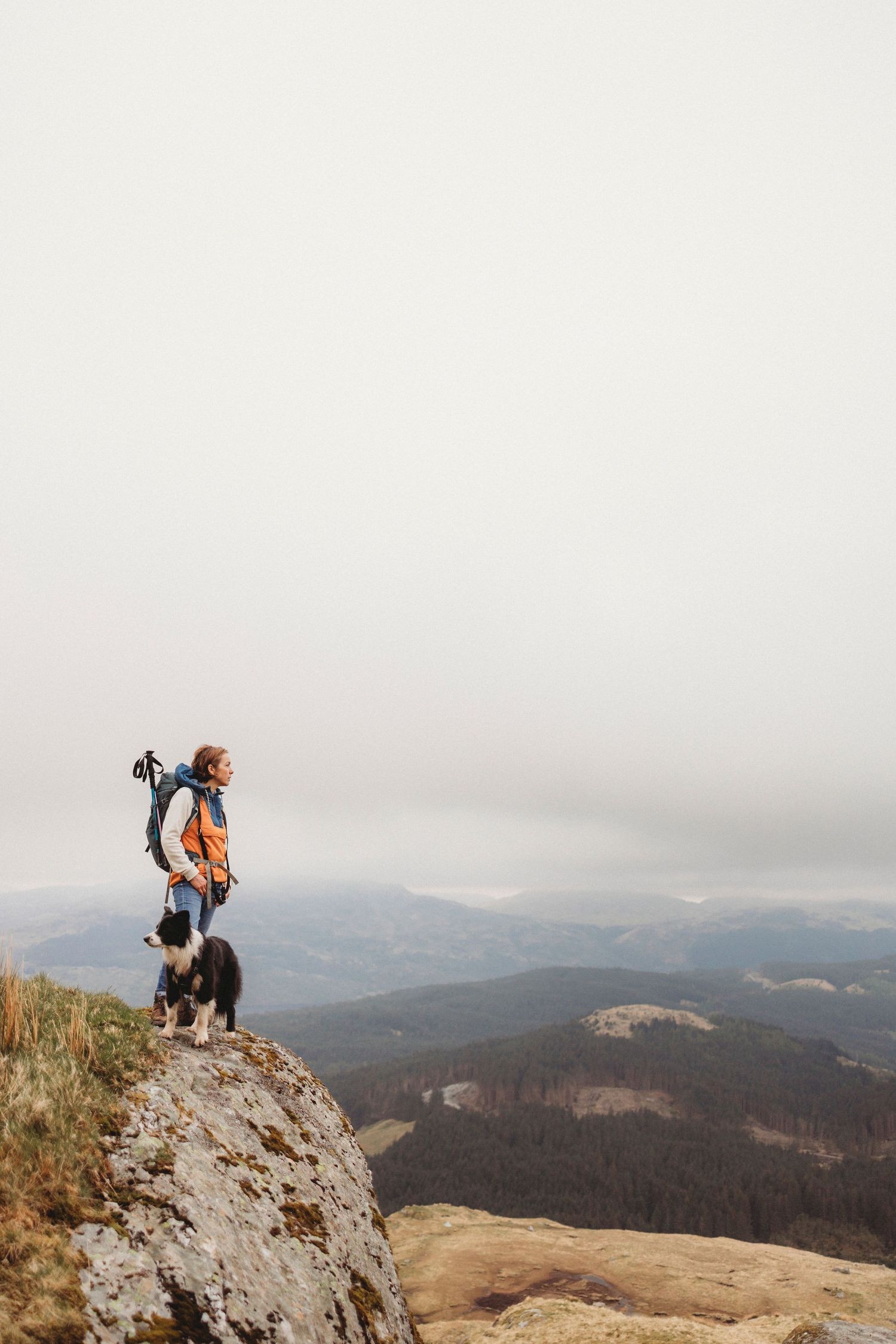 Hiker and dog standing on rocky mountain summit overlooking misty valley landscape.