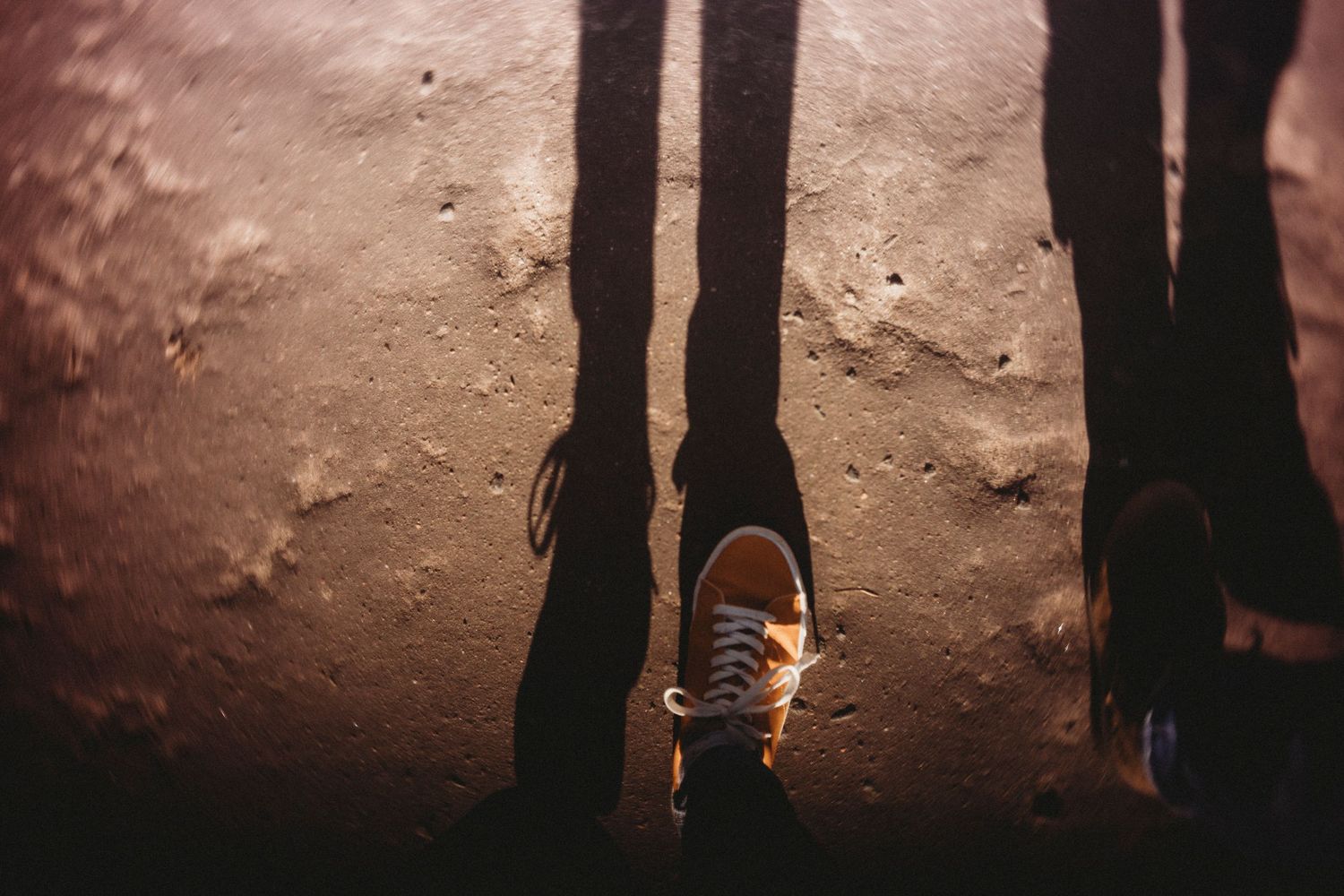 Dramatic silhouette of shoes and shadows on textured ground at sunset.