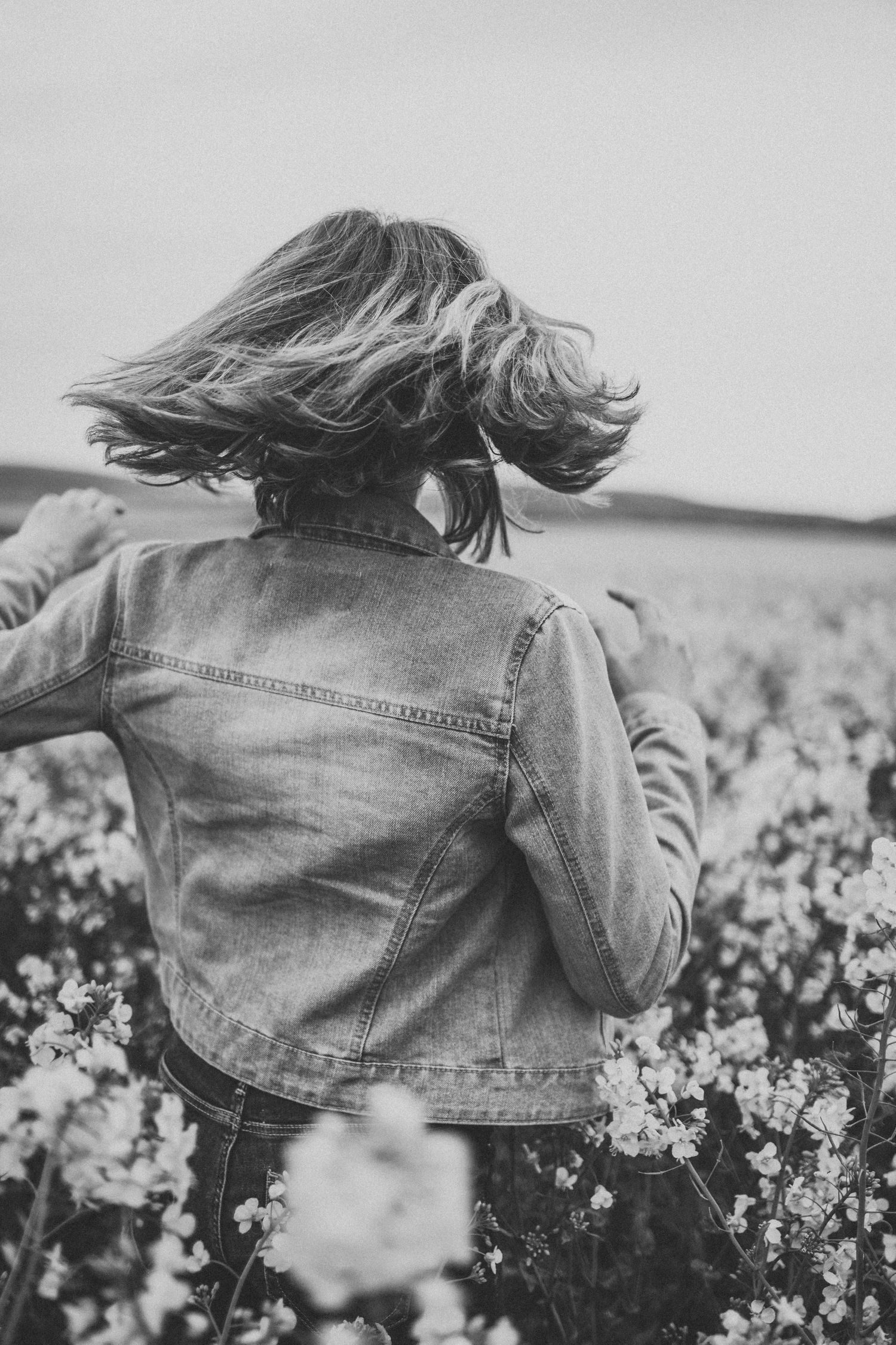 Black and white photo of person with windswept hair wearing denim jacket in flower field.