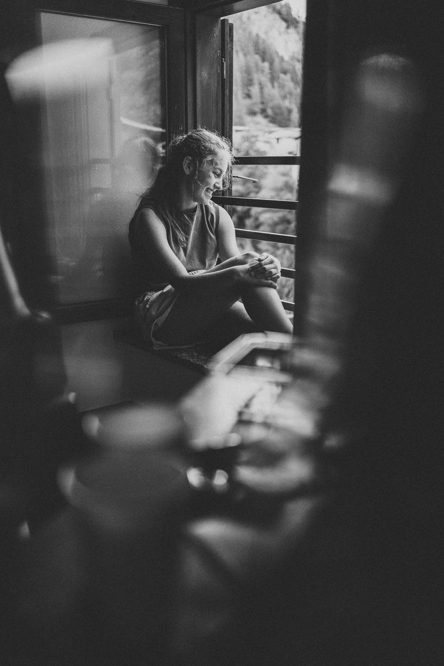 Black and white photo of a smiling woman sitting by a train window, looking outside at a scenic view.