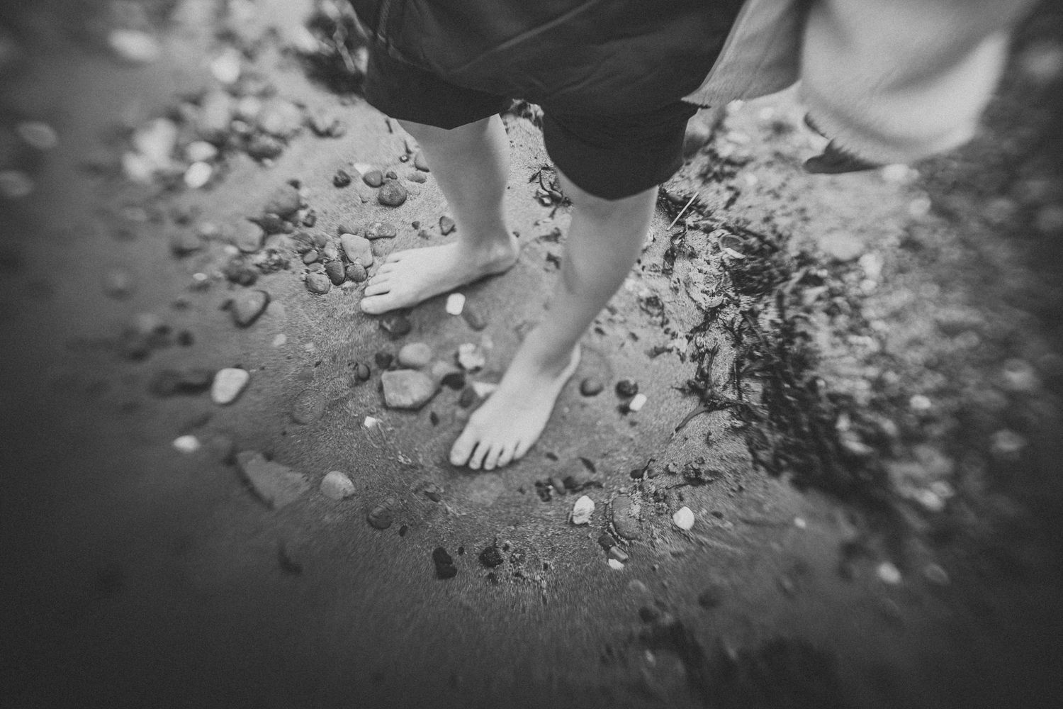 Black and white close-up of bare feet on rocky ground.