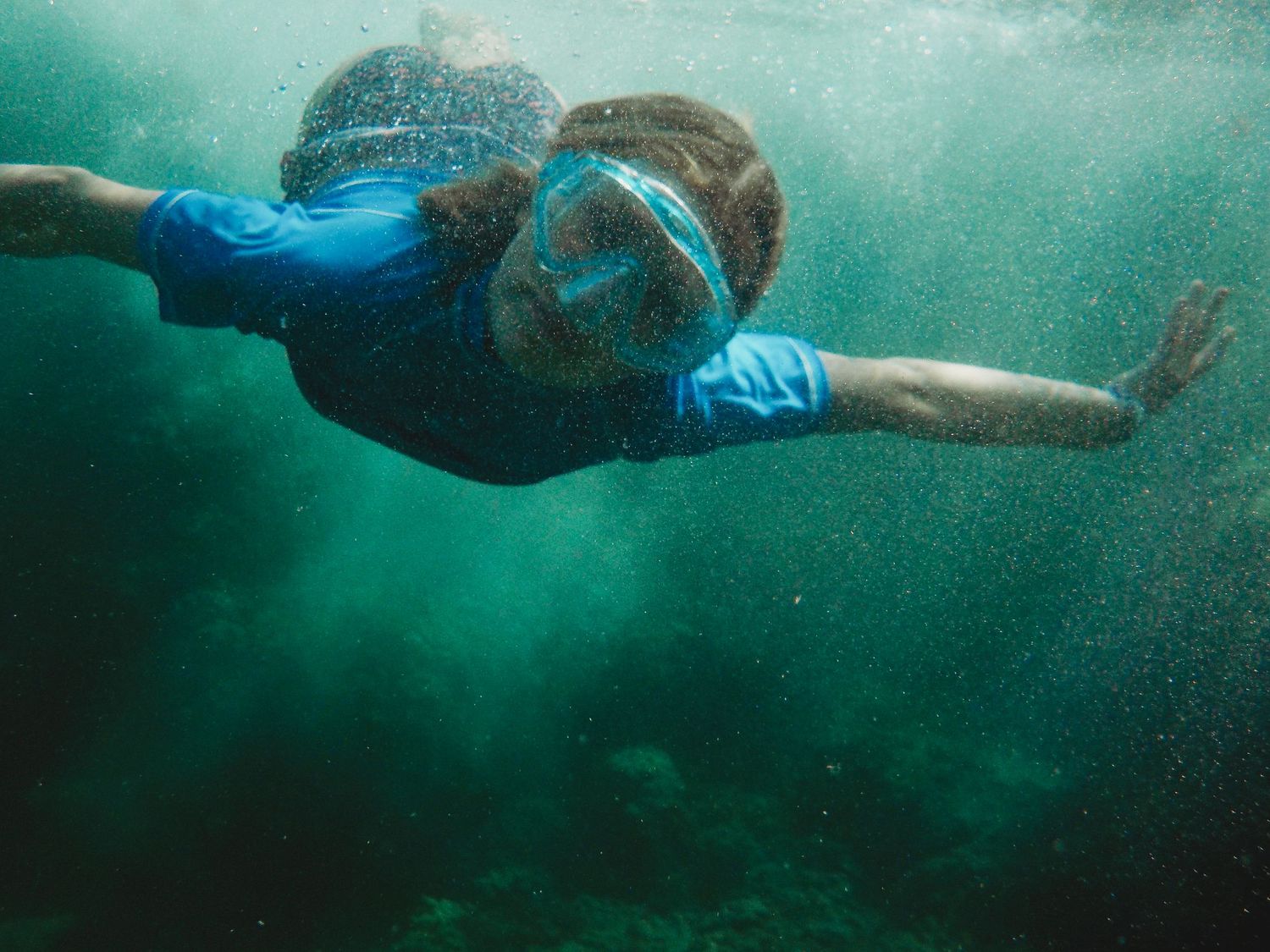 Underwater view of snorkeler swimming in turquoise waters wearing blue wetsuit and mask.