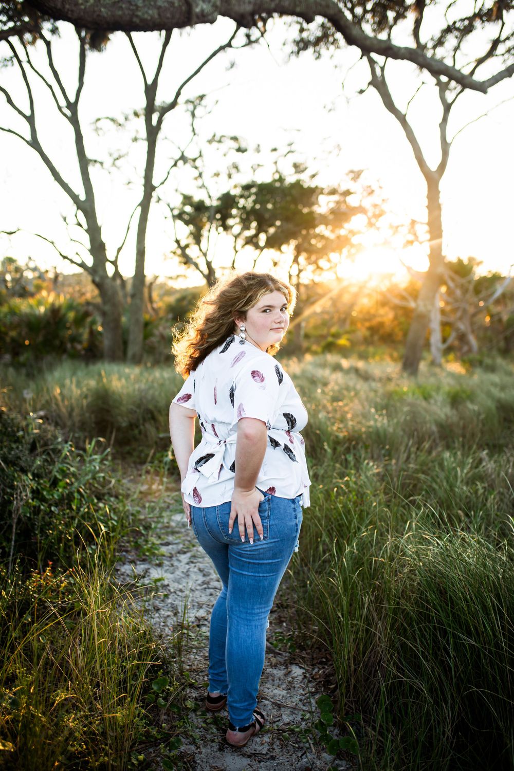 Portrait of a woman in patterned shirt and jeans standing in natural setting during golden hour.