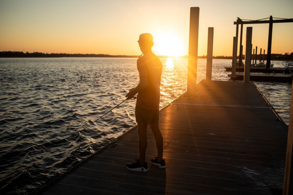 Silhouette of a person standing on a wooden dock at sunset over calm water, golden light reflecting on the lake.