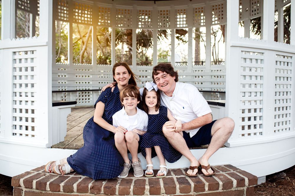A group sits together in a white wooden gazebo during golden hour light, creating a warm family portrait setting.