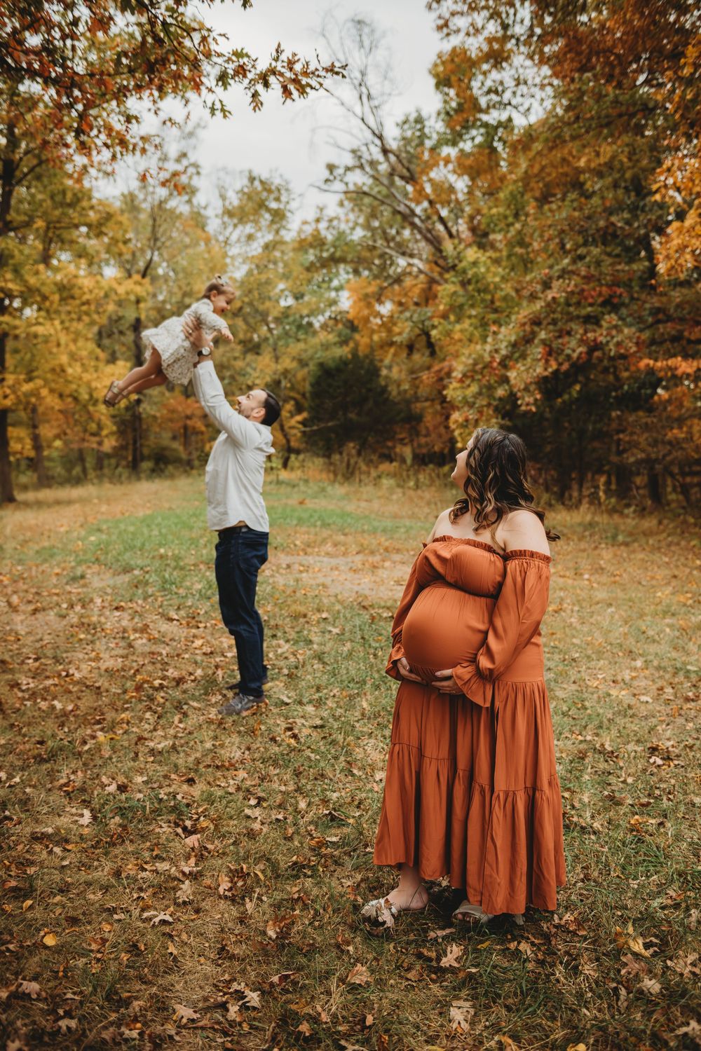 A family enjoying an autumn day in a park with golden foliage as fallen leaves cover the ground.