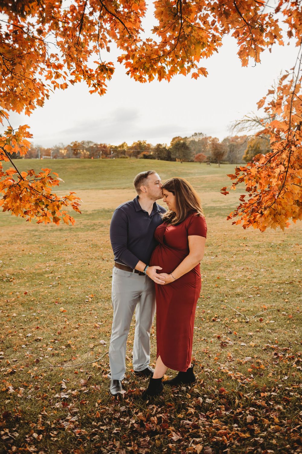 A couple embraces under vibrant orange autumn leaves in a peaceful meadow during golden hour.
