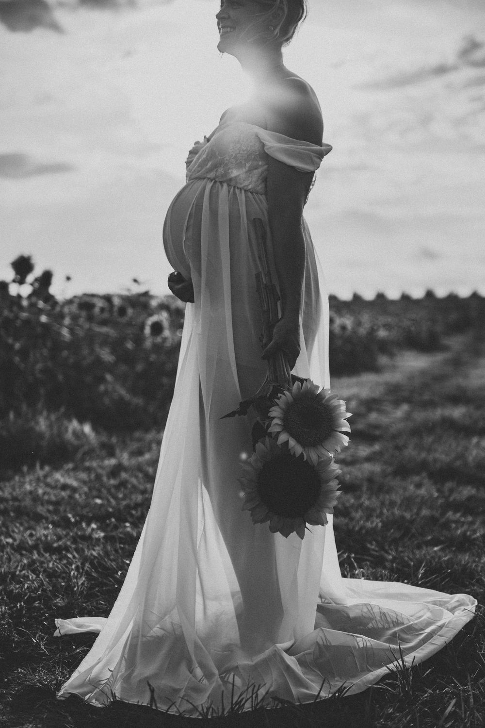Black and white photo series of a flowing white dress in a field with sunflowers at sunset.