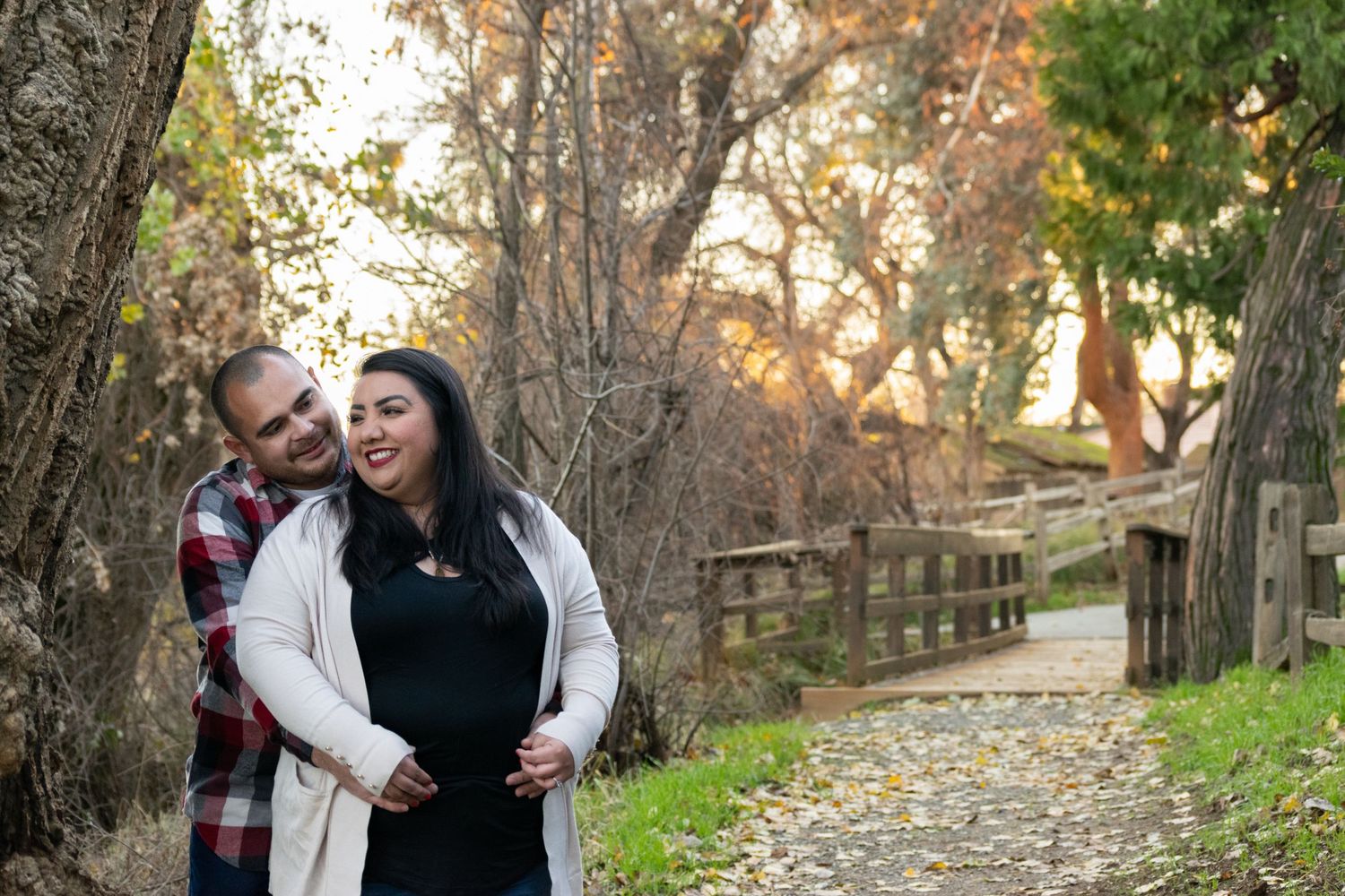 Couple enjoying a tender moment on an autumn path with wooden fence and fall foliage.