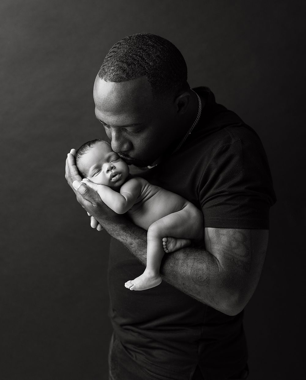 A dramatic black and white series showing a person in a dark shirt holding and kissing a small baby against a black background.
