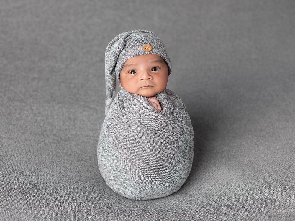 A series of five black and white photos showing a swaddled baby in a gray blanket, progressing from wrapped to unwrapped.
