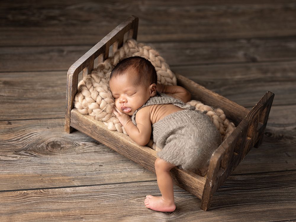 A sleeping newborn baby lies peacefully in a rustic wooden crate on weathered wooden floorboards.