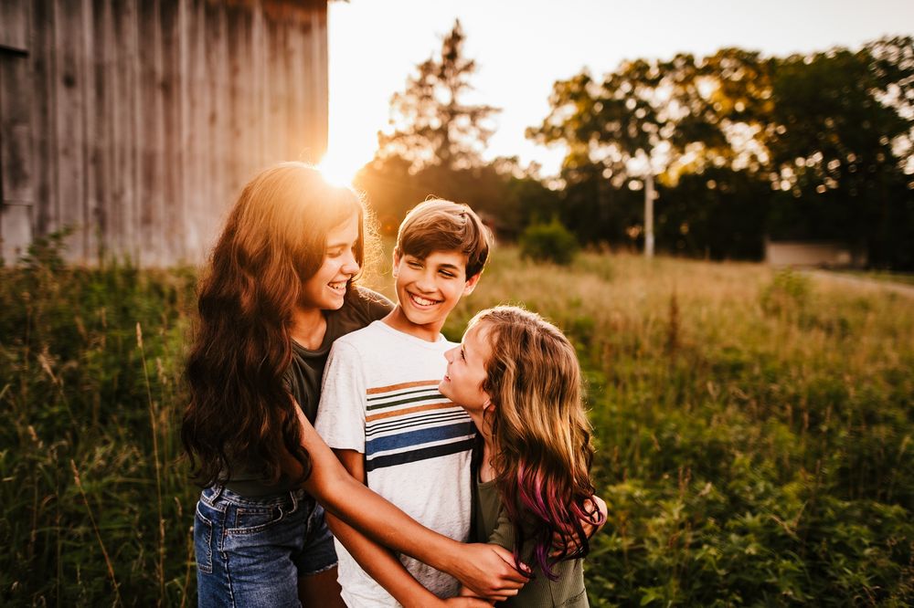 A romantic couple embraces in a sunlit meadow during golden hour as the sun sets behind them creating a warm glow.