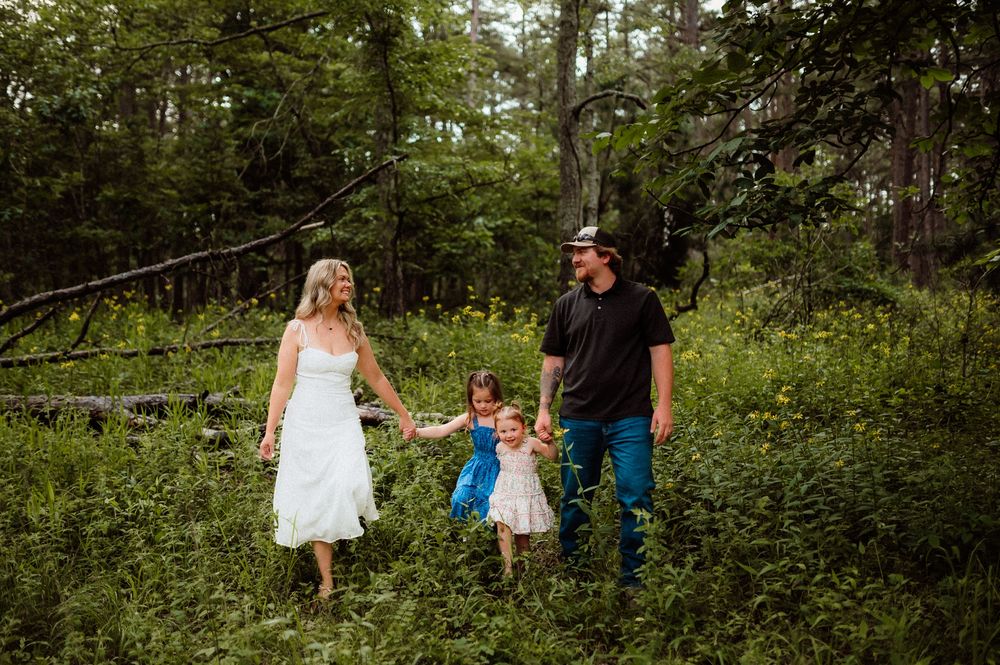 A family holds hands while walking together through lush green woodland on a summer day.