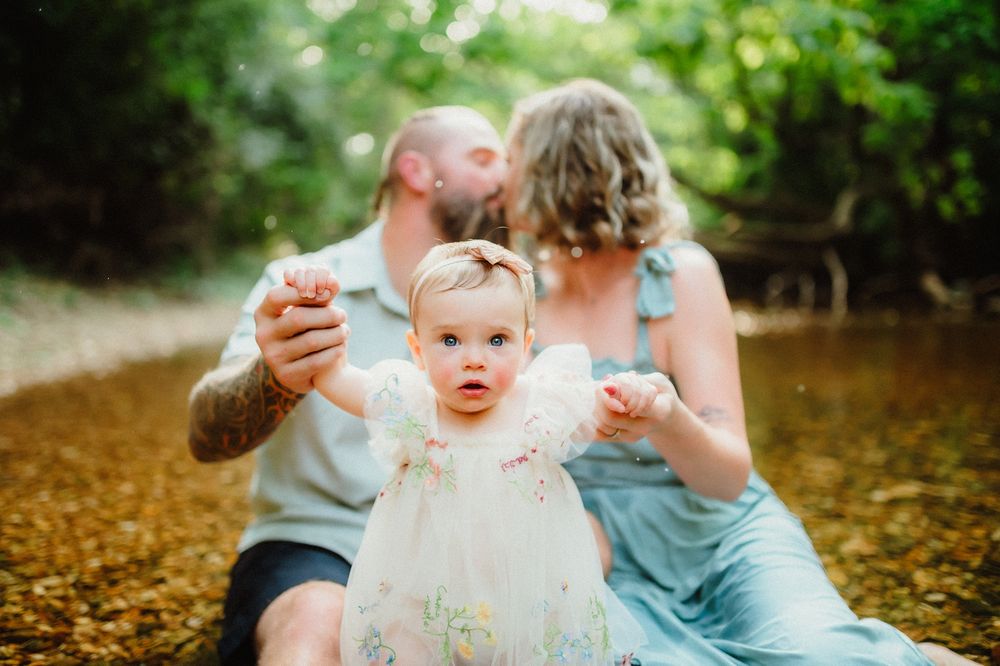 A baby in white dress sits among autumn leaves during an outdoor photo session.