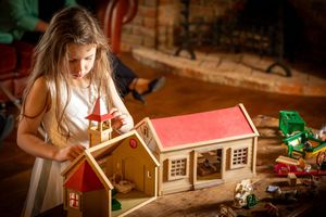 Flower girl playing with a wooden toy sylvanian families farmhouse on a coffee table inside the windmill at Windmill Farm in Burscough.
