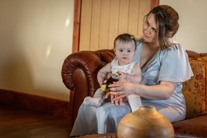 Bridesmaid holding a baby while sitting on a leather sofa inside the windmill at Windmill Farm in Burscough.