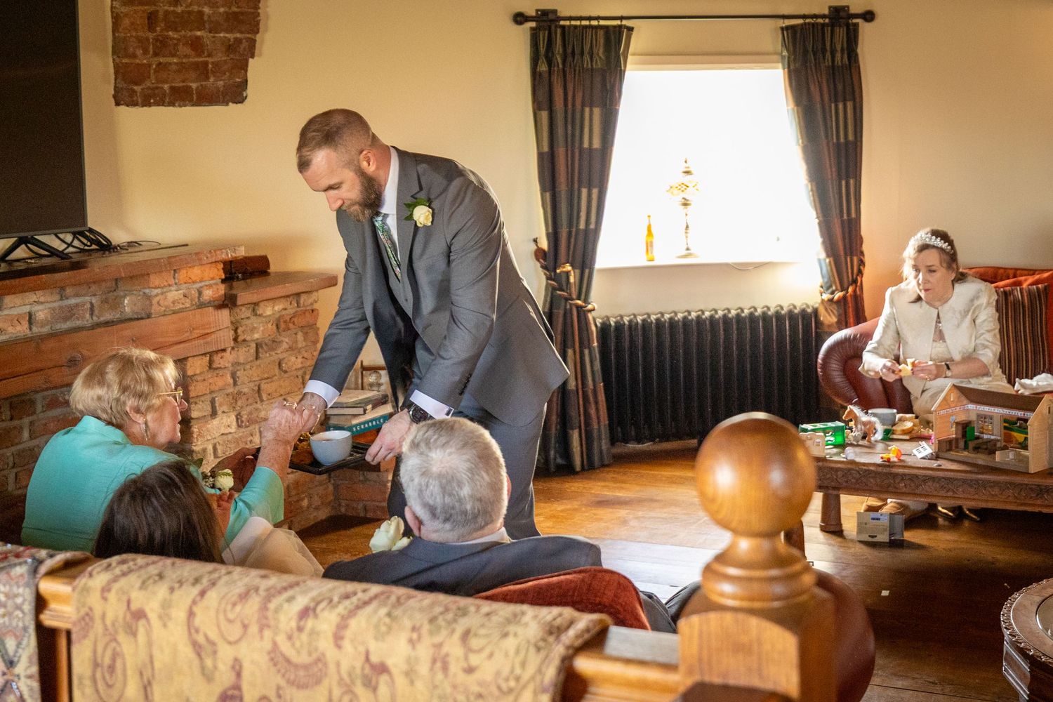 Groomsman serving tea to guests in a cosy room at Windmill Farm in Burscough during a relaxed wedding moment.