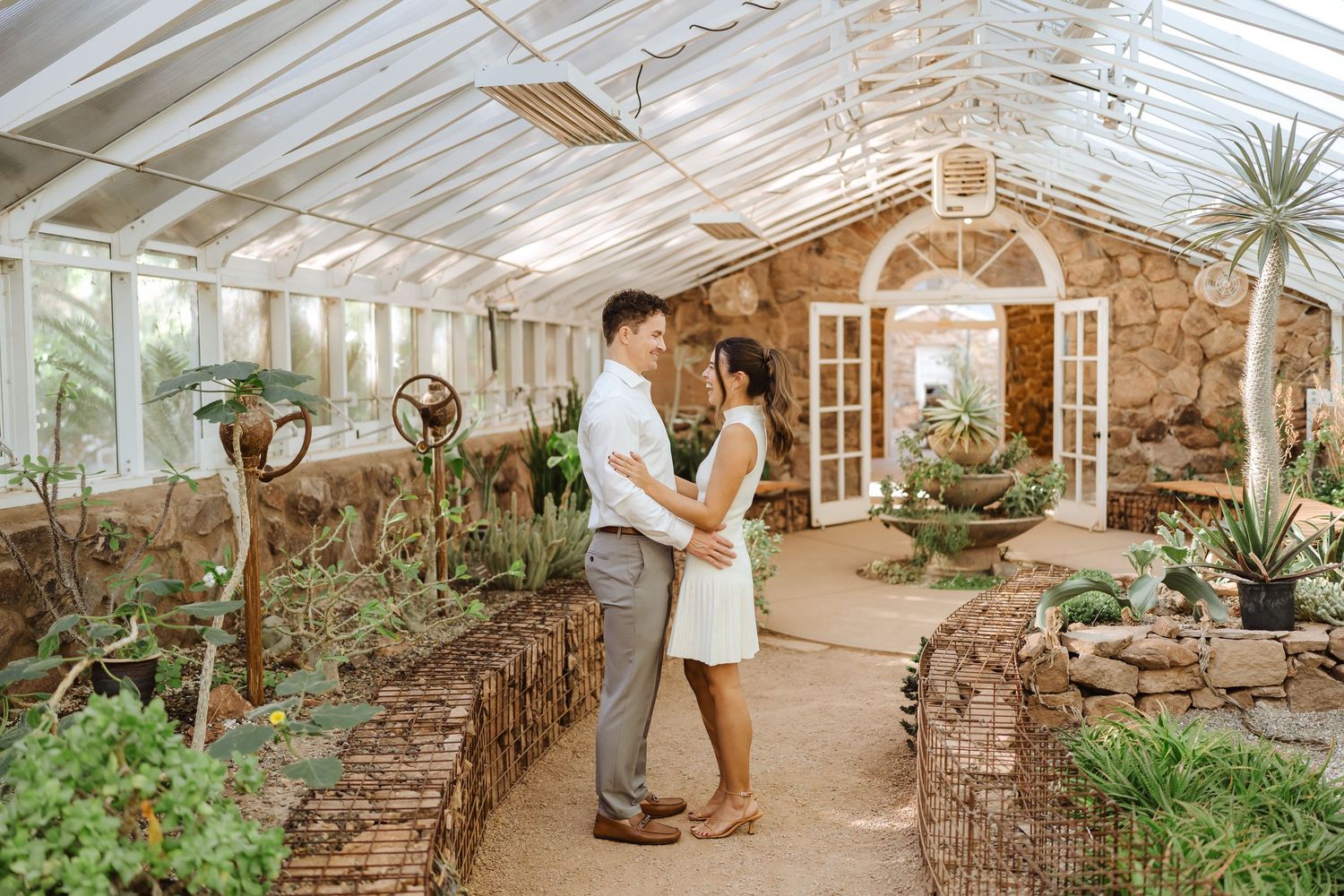 A wedding couple laughs together on a path of desert cacti in a greenhouse at Boyce Thompson Arboretum
