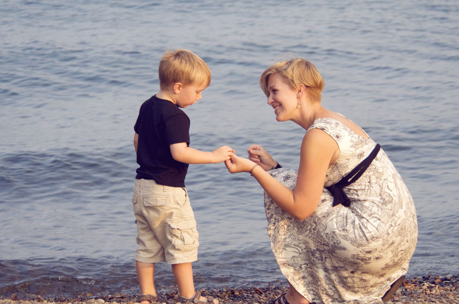 Parent and child share a playful moment collecting shells together along the ocean shoreline.