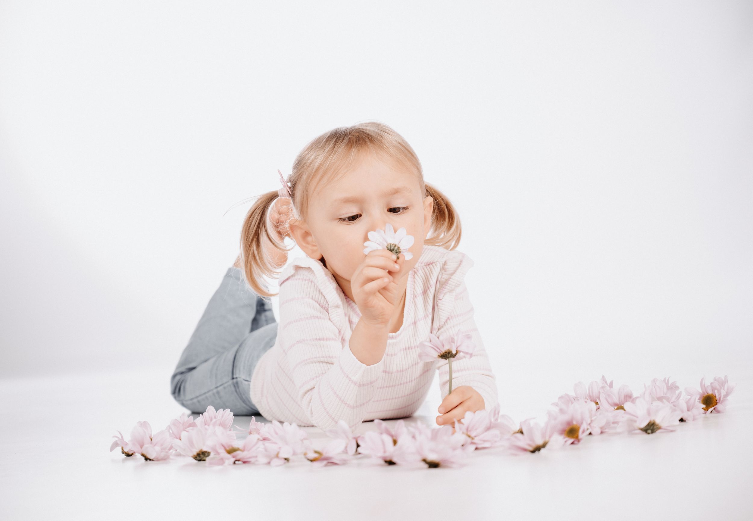 Mädchen liegt auf dem Boden im Fotostudio Gelsenkirchen-Hassel und riecht an einer Blume zwischen Blütenblättern