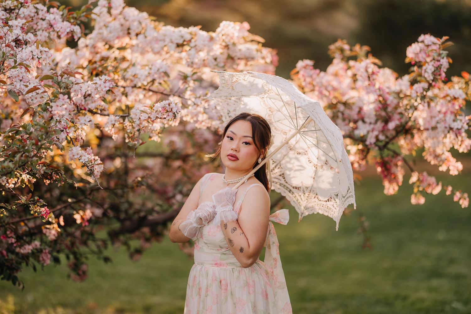 A delicate white lace parasol stands out against blooming pink cherry blossoms in a dreamy spring garden setting.